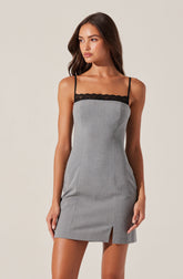 A woman is wearing a sleeveless dress with thin black spaghetti straps and a black lace trim along the top. The dress is primarily light gray with a small slit at the front hem, and it has a fitted silhouette.